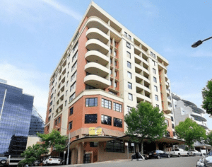 A modern multi-story apartment building with balconies and cars parked along the street.