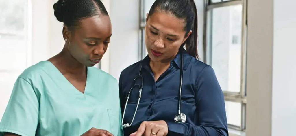 Two healthcare professionals discussing medical monitoring in a bright, clinical setting.