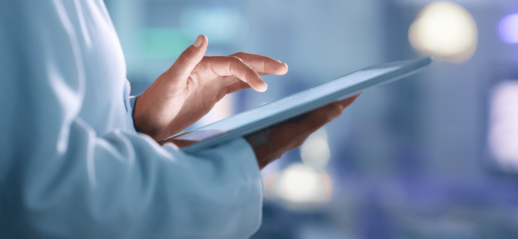 Person in a lab coat using a digital tablet for biostatistics in a modern, bright setting.