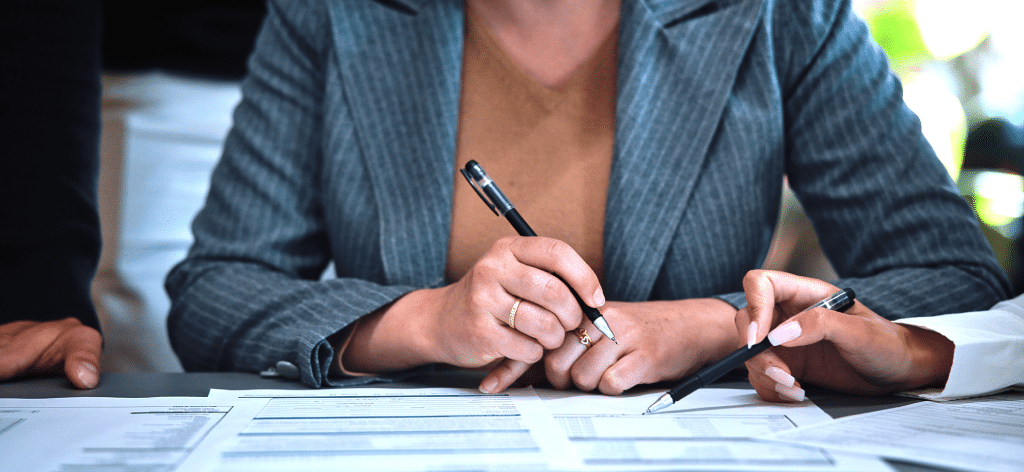 Two people conduct Quality Assurance, reviewing and writing on documents at a desk.